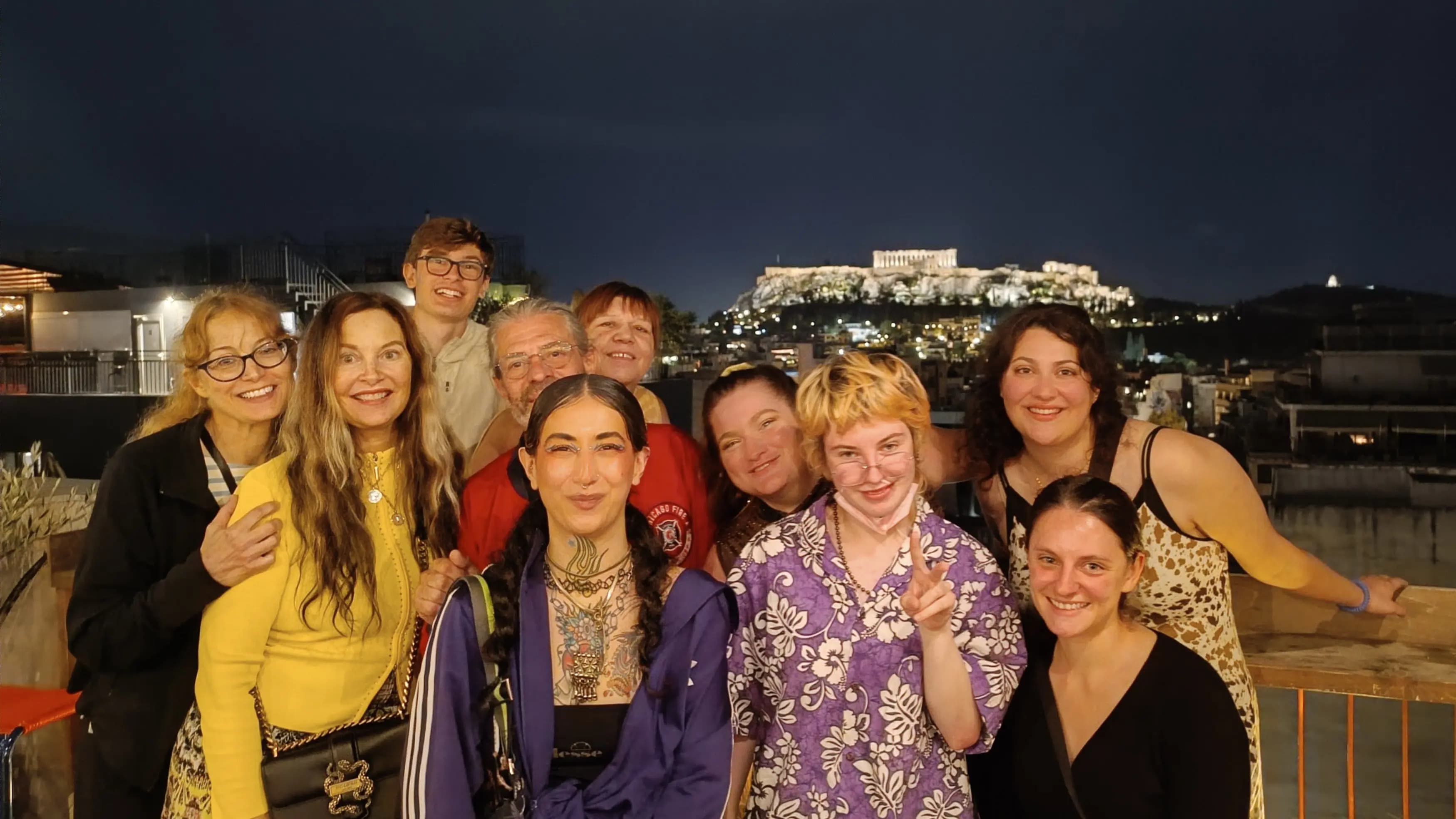 Friends enjoying rooftop pub crawl experience with illuminated Acropolis monument in background